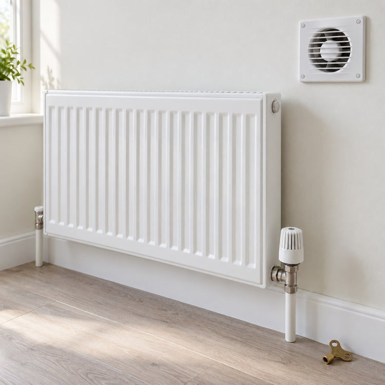 A white panel radiator with a thermostatic valve on a pale wall, with a small extractor fan and a radiator key beside it