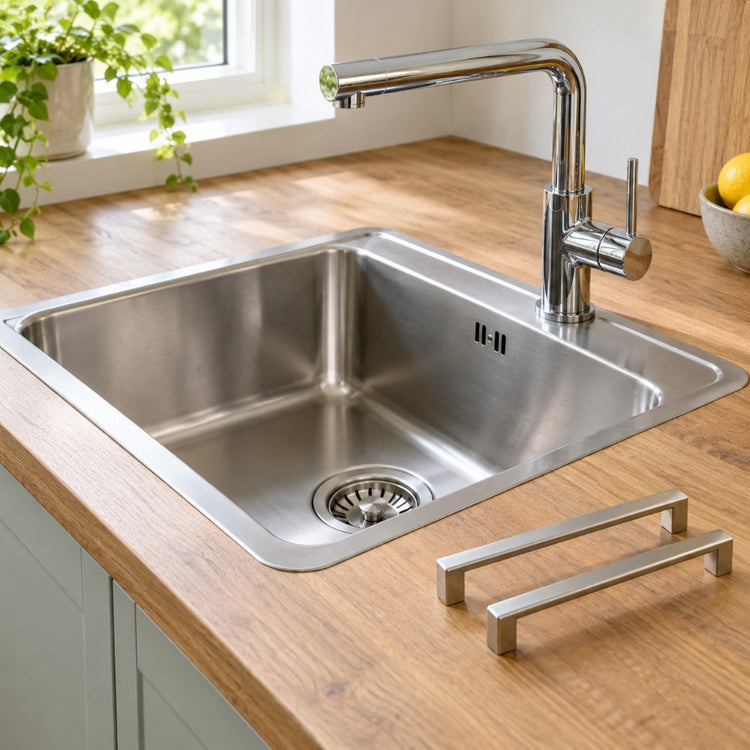 A stainless steel kitchen sink with a chrome mixer tap set into a wooden worktop, with cabinet handles laid beside it