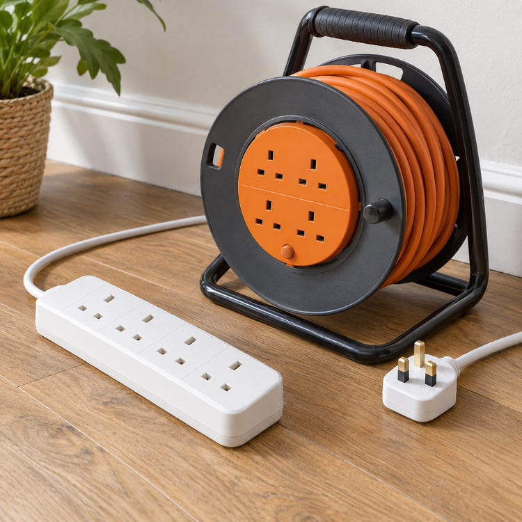 A white four-gang extension lead, a cable reel and a three-pin plug on a wooden floor beside a skirting board