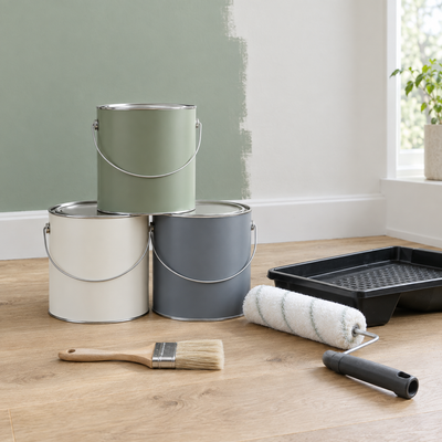 Stack of interior paint tins with roller and brush on an oak floor